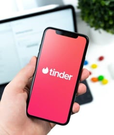 Hand holding a smartphone displaying the Tinder logo on a pink screen. Hand holding a smartphone displaying the Tinder logo on a pink screen.